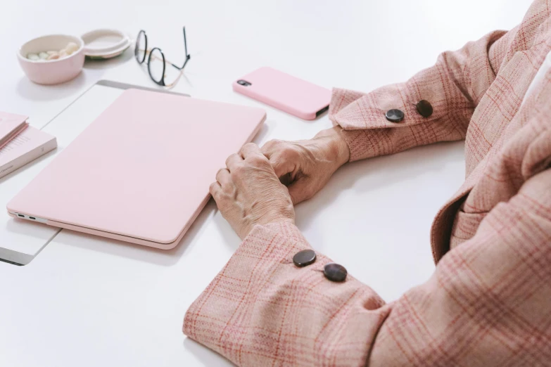 a woman sitting at a table with a pink laptop, by Carey Morris, trending on pexels, elderly woman, holding arms on holsters, rectangle, on a white table