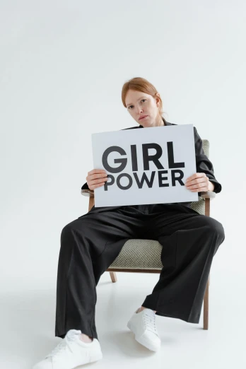 a woman sitting in a chair holding a sign that says girl power, trending on pexels, feminist art, ( redhead, on a gray background, power stance, kirsi salonen
