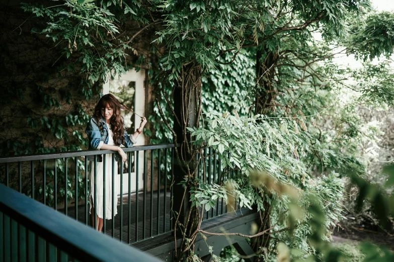 a woman standing on a balcony next to a tree, a photo, unsplash, overgrown with lush vines, cozy treehouse bedroom, profile image, girl with brown hair
