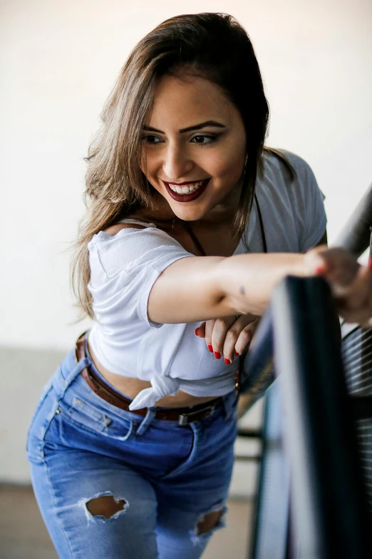 a woman leaning on a rail and smiling, trending on pexels, happening, wearing jeans, young middle eastern woman, cheeky smile with red lips, smiling down from above