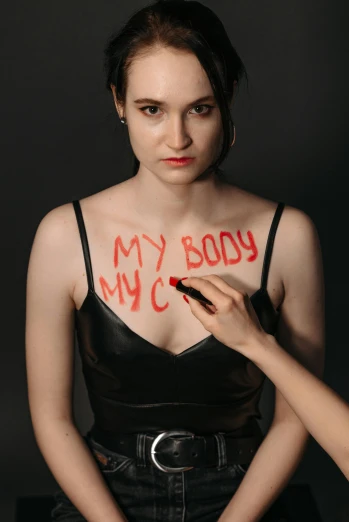 a woman with red writing on her chest, an album cover, inspired by Nan Goldin, feminist art, natalia dyer, bodypaint, rachel weisz portrait, promotional image