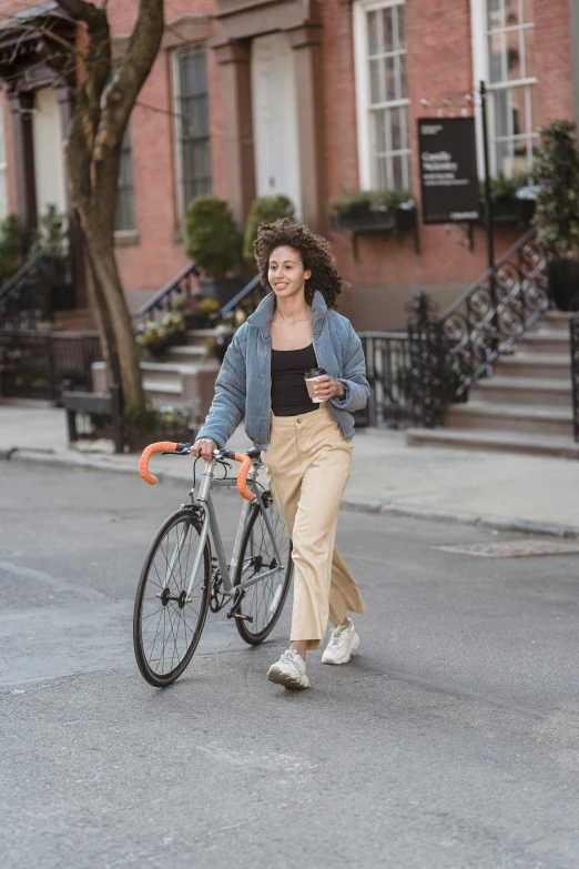 a woman is walking her bike down the street, by Nina Hamnett, happening, brown pants, curly haired, sydney sweeney, industries