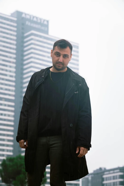 a man standing in front of a tall building, an album cover, inspired by Nadim Karam, he is wearing a black trenchcoat, anton fedeev, thicc, photographed for reuters