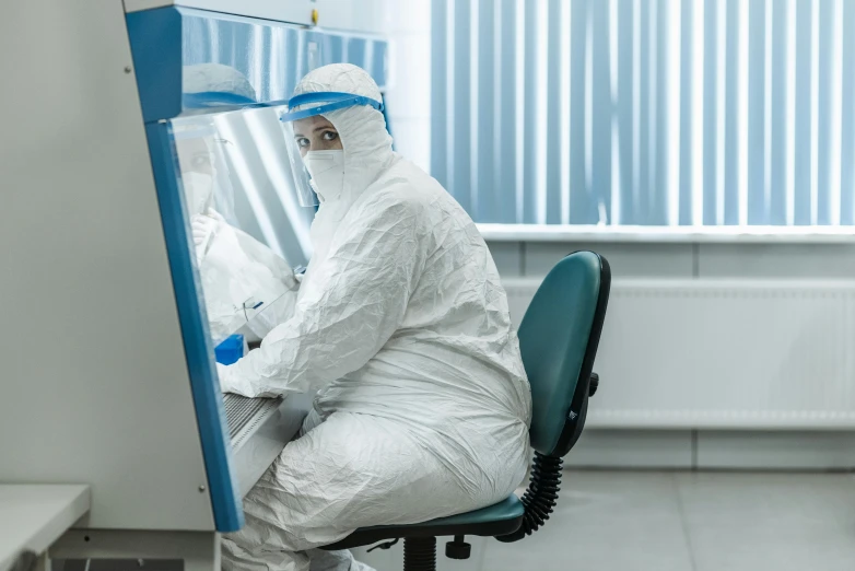 a man in a protective suit sitting at a desk, by Adam Marczyński, shutterstock, private press, on a advanced lab, in australia, biomaterial, knee