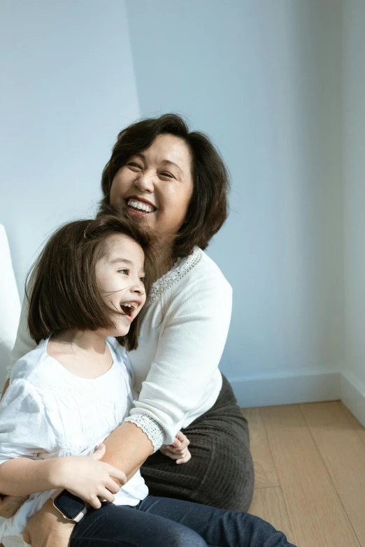 a woman sitting next to a little girl on the floor, inspired by Cui Bai, pexels contest winner, head bent back in laughter, asian descent, plain background, ethnicity : japanese