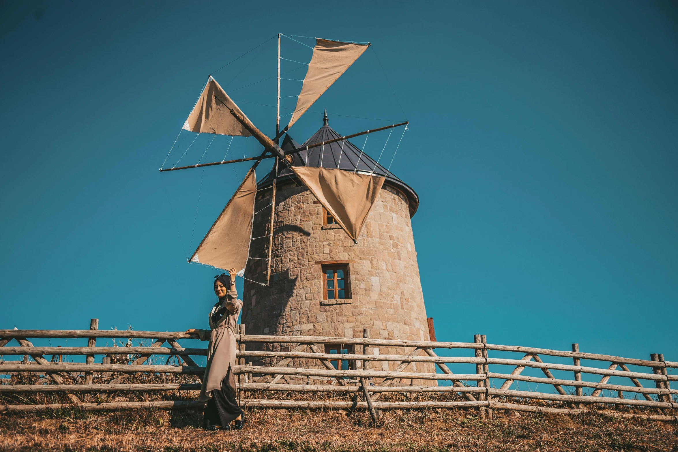 a man standing next to a windmill on top of a hill, a portrait, inspired by Francesco Hayez, unsplash contest winner, sqare-jawed in medieval clothing, girl of the alps, beige, museum quality photo