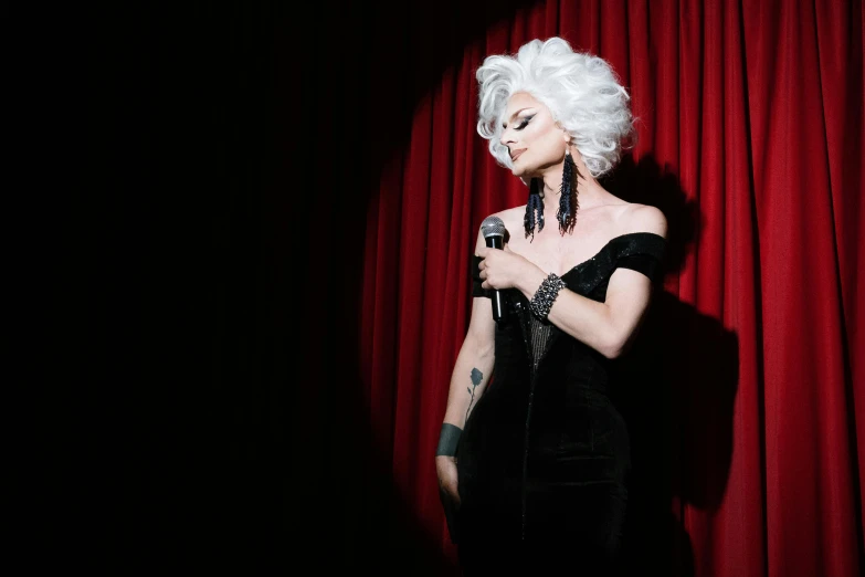 a woman in a black dress holding a microphone, an album cover, pexels, powdered wig, [ theatrical ], danny fox, queer