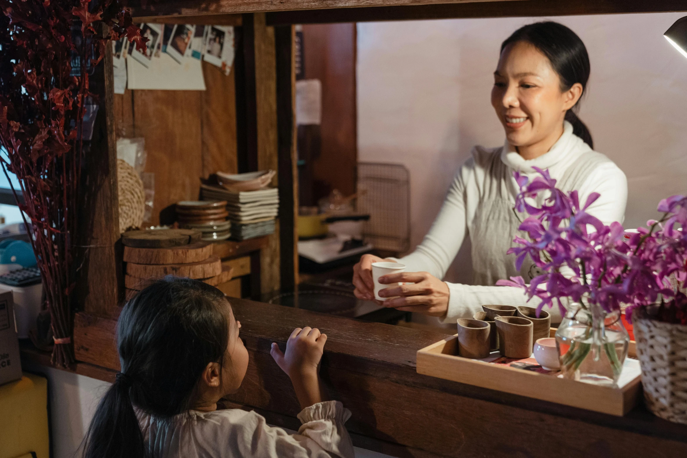 a woman sitting at a counter next to a little girl, inspired by Cui Bai, pexels contest winner, flower shop scene, film still promotional image, an escape room in a small, japanese heritage