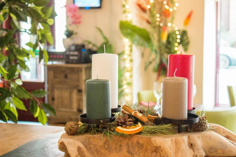 a group of three candles sitting on top of a wooden table, colorful accents, evergreen branches, arrendajo in avila pinewood, indoor scene