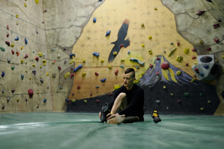 a man sitting on the ground in front of a climbing wall, avatar image, max bedulenko, indoor picture, photographed for reuters