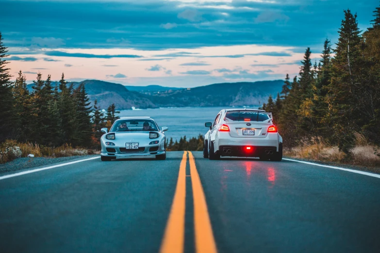 two cars on a road with mountains in the background, a picture, by Drew Tucker, pexels contest winner, lyco art, quebec, aggressive stance, flashing lights, lined up horizontally