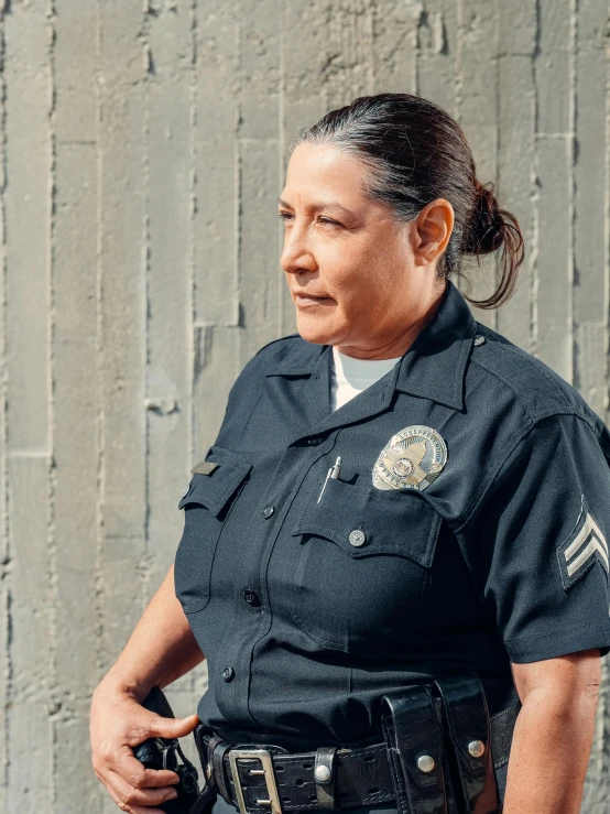 a woman in a police uniform standing in front of a wall, by Alison Geissler, danny trejo, portrait image