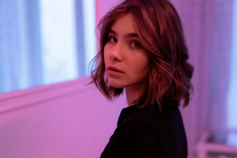 a woman standing in front of a window in a room, an album cover, inspired by Elsa Bleda, trending on pexels, photorealism, madison beer girl portrait, wavy short hazel hair, glowing magenta face, imogen poots