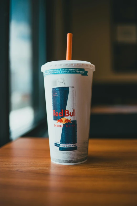 a red bull cup sitting on top of a wooden table, white neon wash, with a straw, teal and orange, full-figure