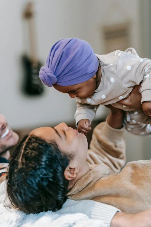 a man laying on top of a bed holding a baby, pexels contest winner, renaissance, wearing a purple cap, varying ethnicities, manuka, above the family room