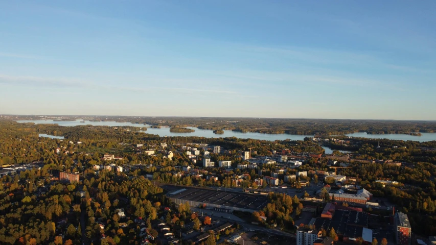 an aerial view of a city surrounded by trees, by Veikko Törmänen, unsplash, hurufiyya, lake in the background, helicopter footage over city, late afternoon, maintenance photo