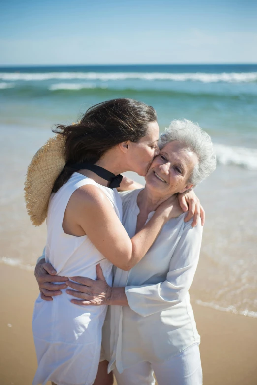 a woman kissing an older woman on the beach, by Elizabeth Durack, unsplash, happening, lush surroundings, album, white, queen