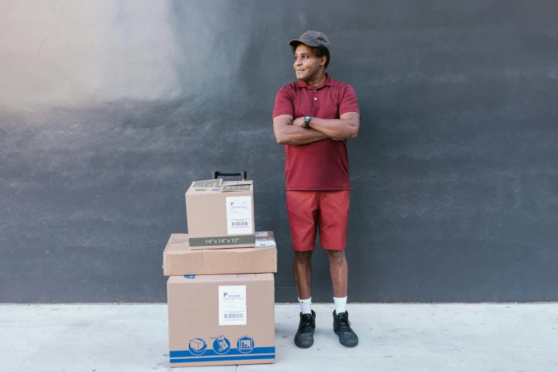 a man standing next to a stack of boxes, a portrait, by Carey Morris, pexels contest winner, maroon, avant designer uniform, wearing shorts and t shirt, samuel l jackson