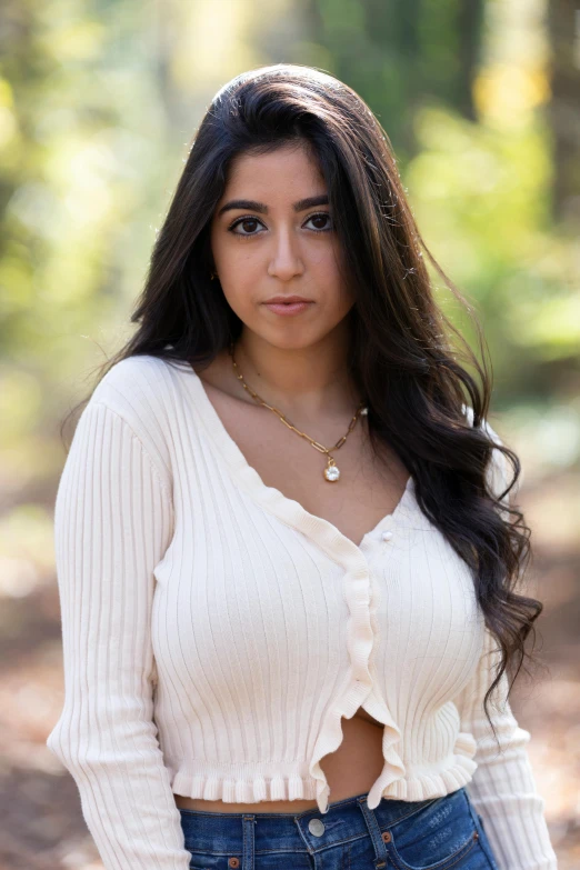 a woman posing for a picture in the woods, an album cover, trending on pexels, renaissance, wearing white v - neck top, young middle eastern woman, wearing a cardigan, close up bust shot