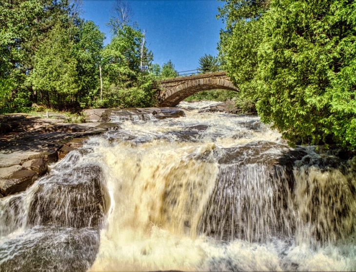 a waterfall with a bridge in the background, by Jesper Knudsen, pexels contest winner, hurufiyya, “ iron bark, minn, beautiful weather, thumbnail