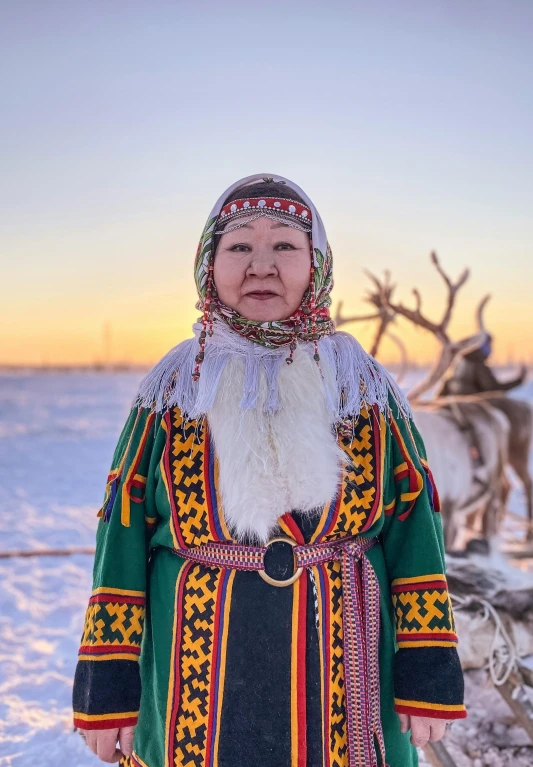 a woman standing in the snow next to reindeers, by Jesper Knudsen, pexels contest winner, symbolism, colourful clothing, indigenous man, front portrait, official government photo