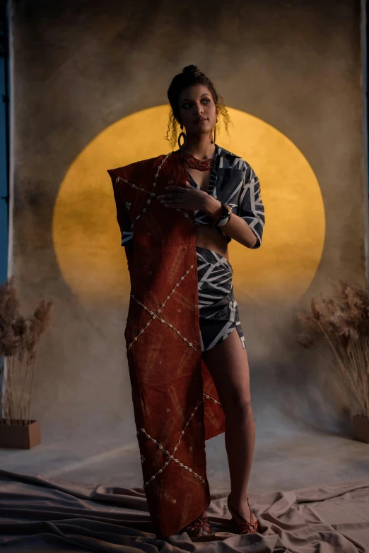 a woman standing in a room holding a blanket, trending on pexels, afrofuturism, in front of a full moon, at a fashion shoot, batik, ( ( theatrical ) )