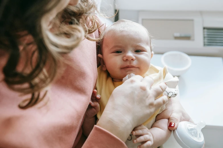 a woman holding a baby in her arms, by Emma Andijewska, pexels, drinking cough syrup, closeup - view, high quality upload, babies in her lap
