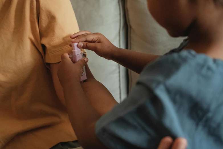 a close up of a person putting something on a person's arm, a child's drawing, carrying a bottle of perfume, manuka, supportive, casually dressed