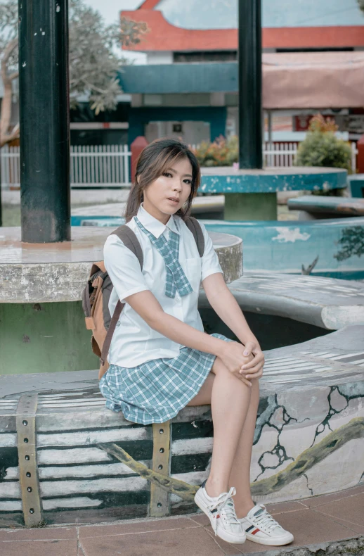 a woman sitting on a bench next to a fountain, a portrait, trending on cg society, wearing school uniform, malaysian, 5 0 0 px models, low quality photo