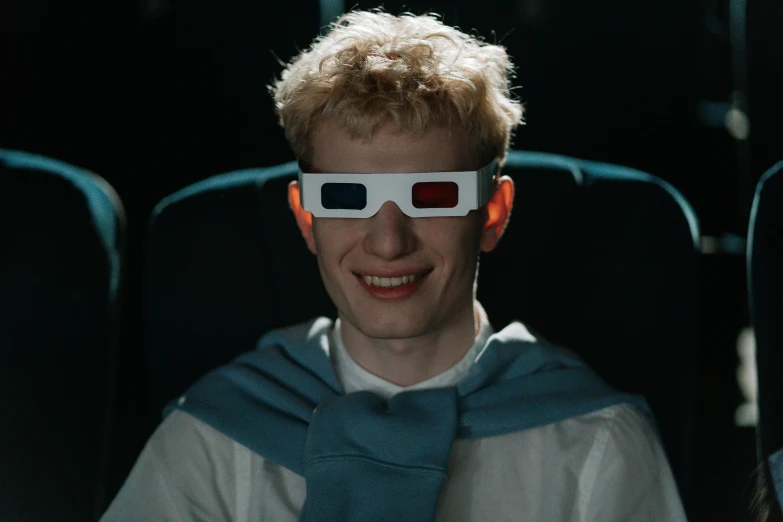a man sitting in a movie theater wearing 3d glasses, a hologram, by Ryan Pancoast, featured on reddit, video art, young blonde boy fantasy thief, cute slightly nerdy smile, cinestill colour, cinematic promo material