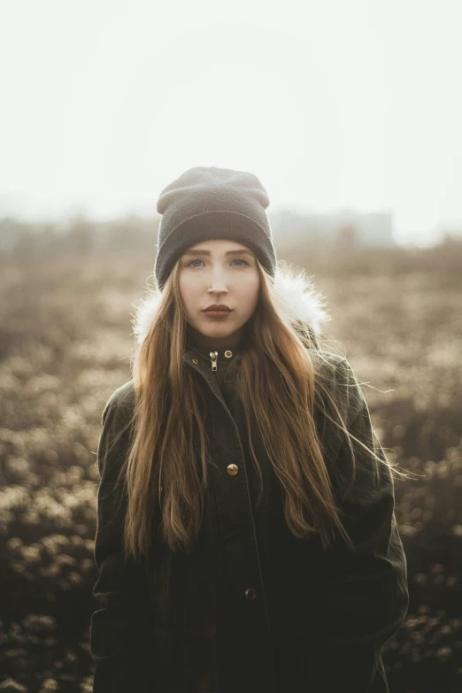 a woman standing in a field wearing a hat, a picture, inspired by Elsa Bleda, trending on pexels, backlit shot girl in parka, frowning, 🤤 girl portrait, teenage