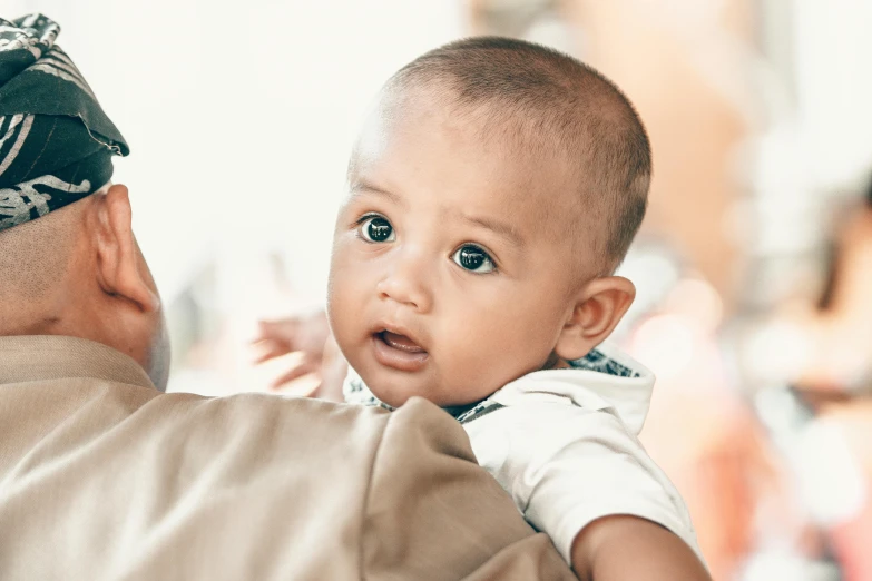 a man holding a baby in his arms, pexels contest winner, hurufiyya, mixed race, serious focussed look, brown, dynamic closeup