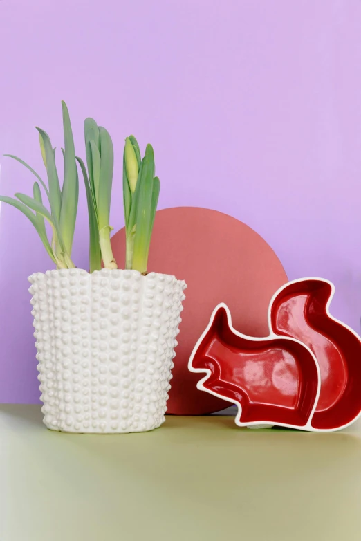 a white vase sitting on top of a table next to a plant, inspired by Jeff Koons, pop art, whimsical fox, soft red texture, hyacinth, professional product photo