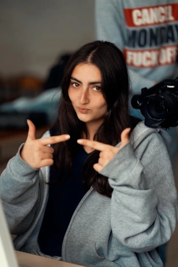 a woman sitting in front of a laptop computer, a picture, inspired by Elsa Bleda, trending on pexels, photorealism, pointing at the camera, black haired girl wearing hoodie, wearing a grey robe, chappie in an adidas track suit