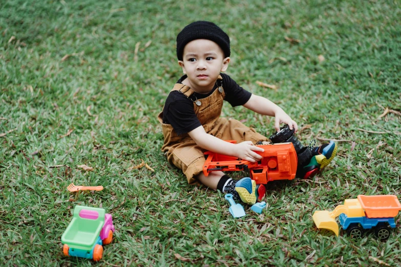 a little boy that is sitting in the grass, the woman holds more toys, with black beanie on head, gen z, construction