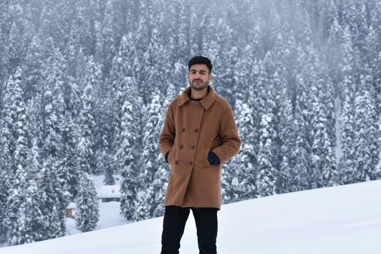 a man standing on top of a snow covered slope, inspired by Abdullah Gërguri, pexels contest winner, hurufiyya, light brown trenchcoat, with slight stubble, daniel ricciardo, thumbnail