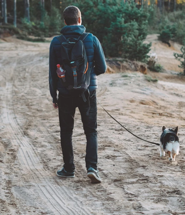 a man walking a dog down a dirt road, a man wearing a backpack, wearing jeans and a black hoodie, thumbnail, snacks