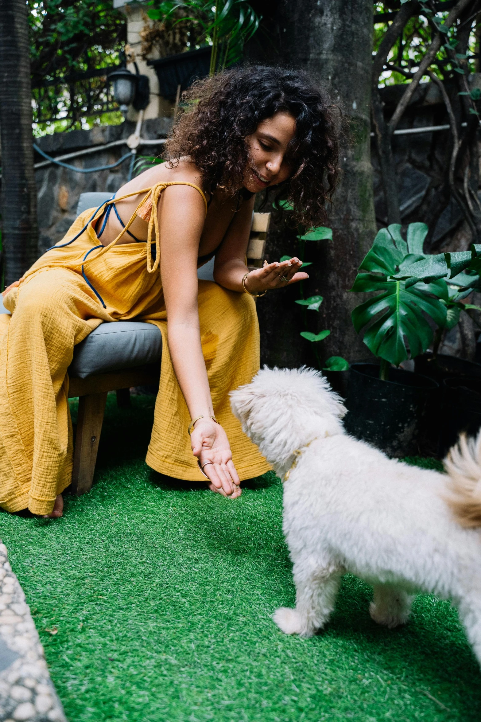 a woman sitting on a bench petting a white dog, pexels contest winner, yellow carpeted, bali, partially cupping her hands, lush green