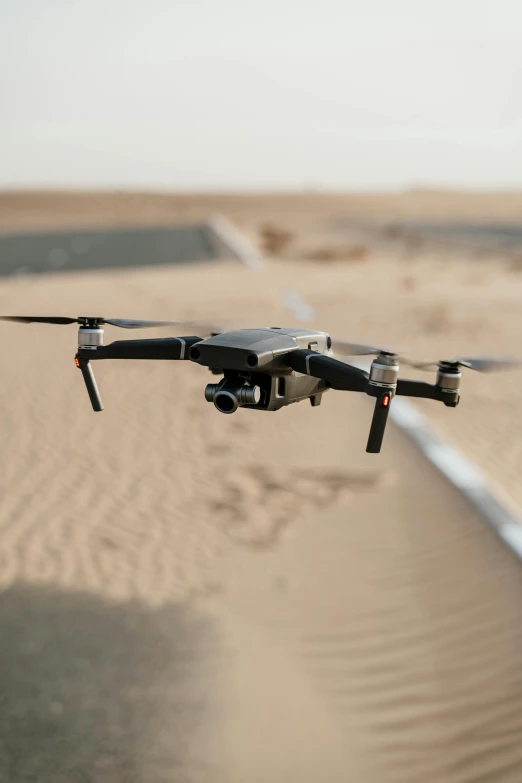 a black drone flying over a sandy beach, pexels contest winner, oman, on a landing pad, electronics, cgi 8k