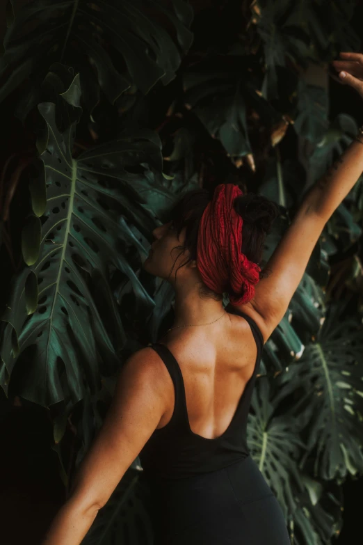 a woman standing in front of a lush green plant, bare back, dark jungle, profile image, arms stretched out