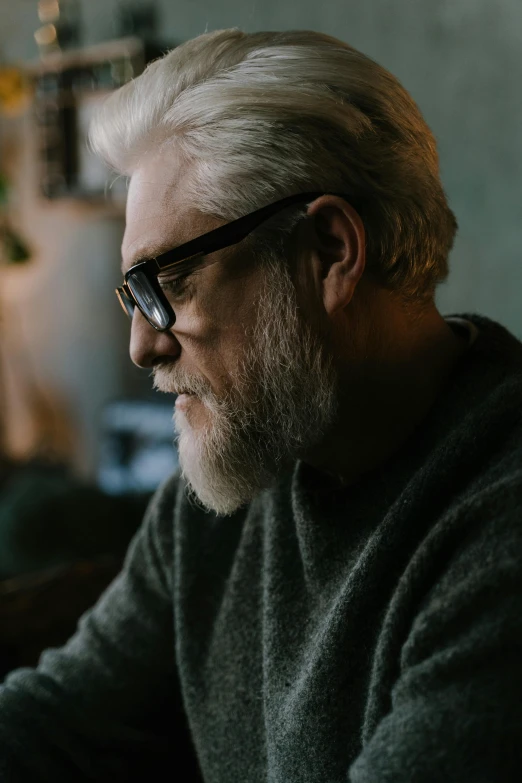 a man sitting at a table using a laptop computer, a character portrait, by Andrew Geddes, trending on pexels, some grey hair in beard, pensive, wearing black frame glasses, jay leno with gray skin