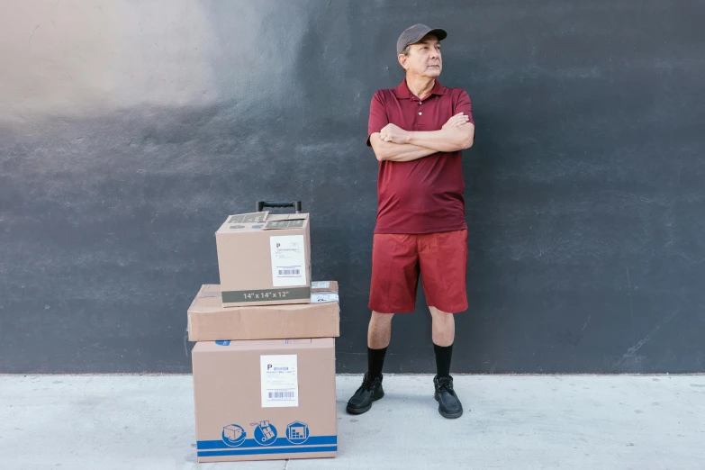 a man standing next to a stack of boxes, a portrait, pexels contest winner, maroon, avant designer uniform, wearing shorts and t shirt, an oldman