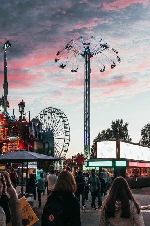 a crowd of people walking down a street next to a ferris wheel, during a sunset, fairground rides, profile image