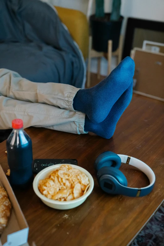 a person laying on a couch next to a box of pizza, an album cover, trending on pexels, eating chips and watching tv, blue pants, foot wraps, bowl filled with food