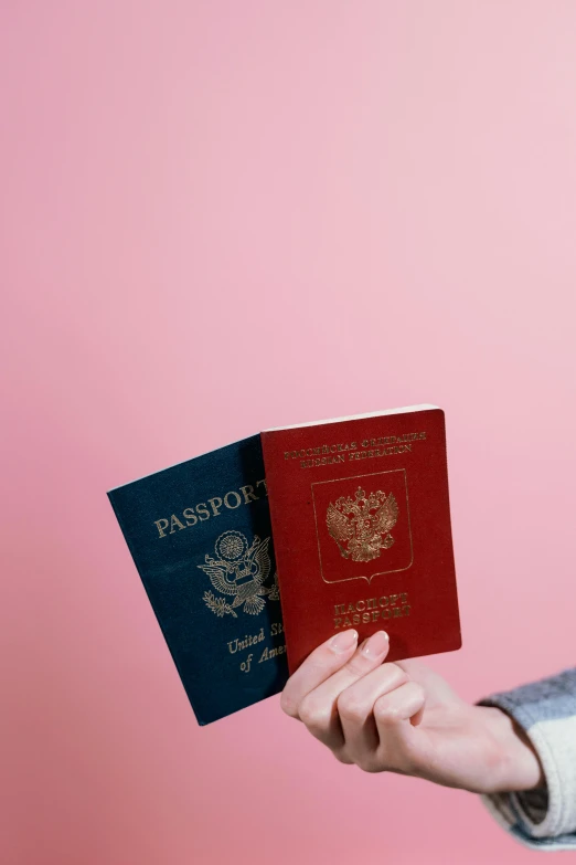 a woman holding two passports in one hand and a passport in the other, an album cover, by Julia Pishtar, trending on unsplash, regionalism, pink and red color scheme, vertical orientation, united states, terry richardson