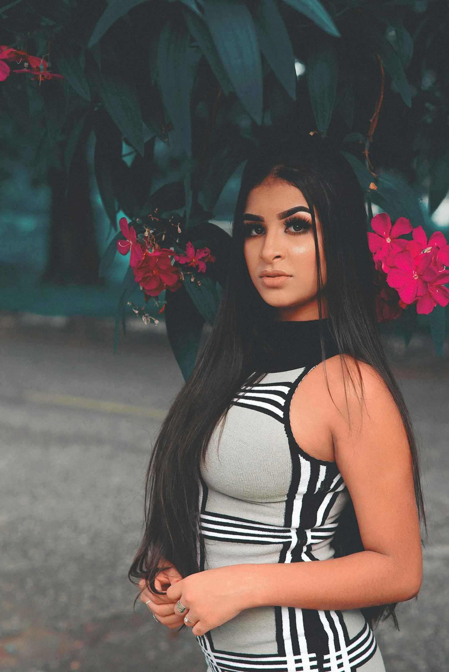 a woman in a black and white dress posing for a picture, long black straight hair, next to a plant, wearing a crop top, tanned ameera al taweel