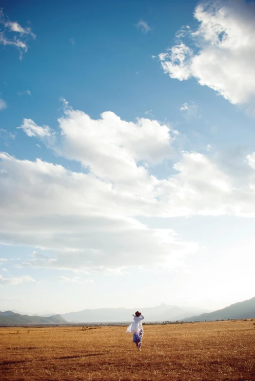 a person in a field flying a kite, by Jessie Algie, unsplash, minimalism, hills and mountains, big clouds, biker, wedding