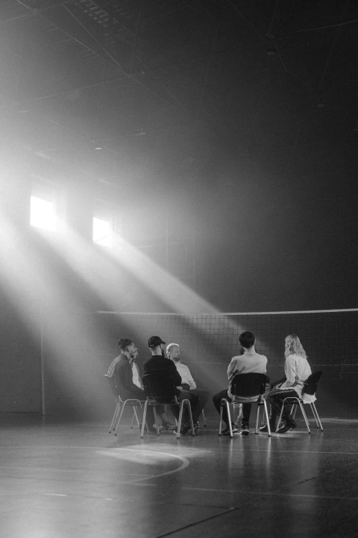 a group of people sitting around a volleyball court, a black and white photo, by Jang Seung-eop, unsplash contest winner, light and space, movie lighting, sittin, alternate album cover, recital