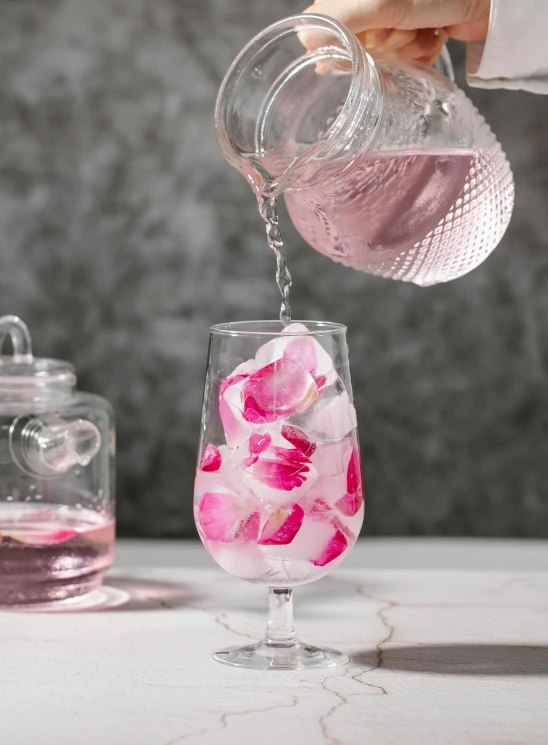 a person pouring pink liquid into a glass, inspired by Rose Henriques, large individual rose petals, ice cubes, highly upvoted, high quality product image”