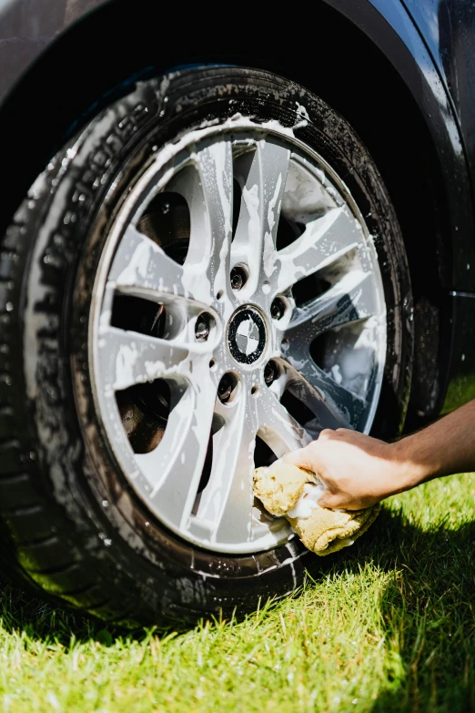a person washing a car with a sponge, paws on wheel, dirt and grawel in air, slick tires, delightful surroundings